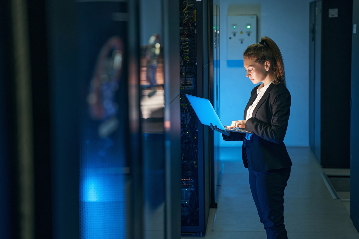 Female engineer working on a laptop beside server racks in a modern server room